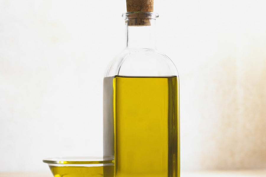 Glass bottle of golden cold-pressed oil with a cork stopper and a small dish of oil beside it