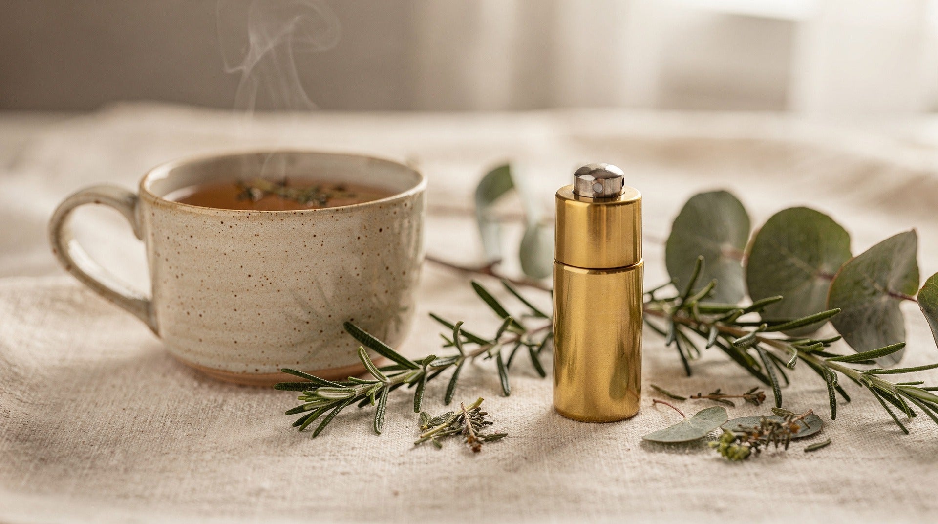 Cup of herbal tea beside a roll-on oil bottle with rosemary and eucalyptus sprigs